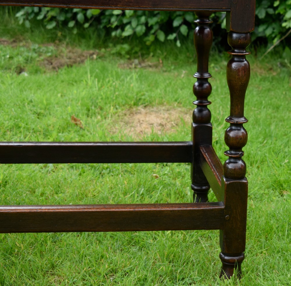 A dark oak 17th-century lowboy table featuring a carved rectangular top, a single carved drawer front with a central brass handle, turned legs, and low wooden stretchers. View IX