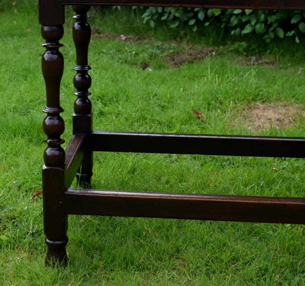 A dark oak 17th-century lowboy table featuring a carved rectangular top, a single carved drawer front with a central brass handle, turned legs, and low wooden stretchers. View X