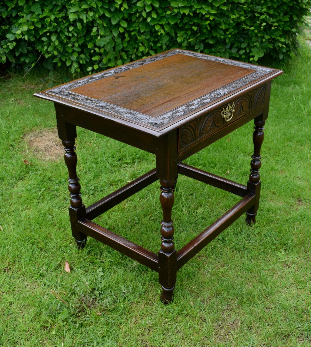 A dark oak 17th-century lowboy table featuring a carved rectangular top, a single carved drawer front with a central brass handle, turned legs, and low wooden stretchers. View XI