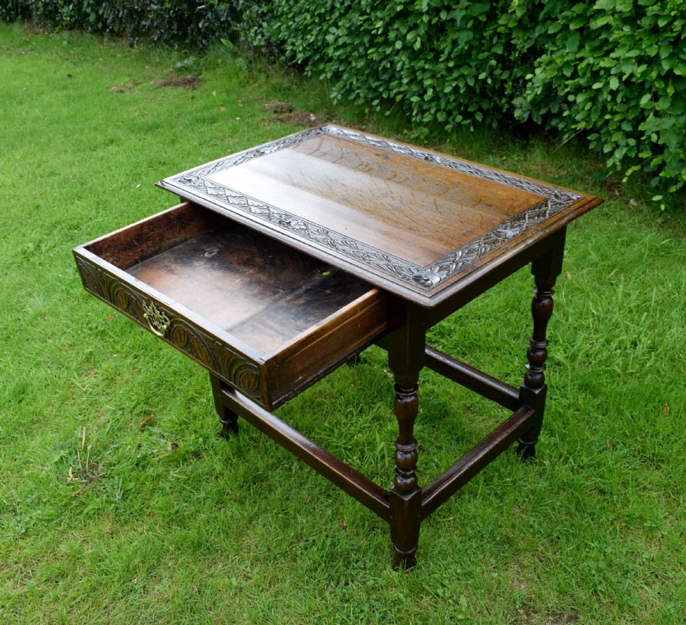 A dark oak 17th-century lowboy table featuring a carved rectangular top, a single carved drawer front with a central brass handle, turned legs, and low wooden stretchers. View XIII