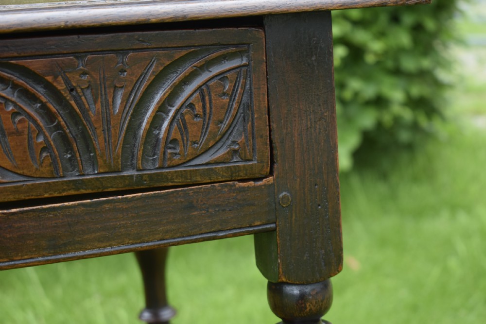 A dark oak 17th-century lowboy table featuring a carved rectangular top, a single carved drawer front with a central brass handle, turned legs, and low wooden stretchers. View XIV
