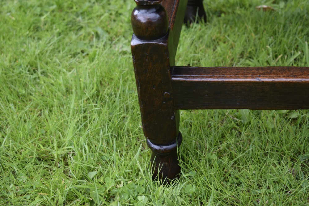 A dark oak 17th-century lowboy table featuring a carved rectangular top, a single carved drawer front with a central brass handle, turned legs, and low wooden stretchers. View XVI