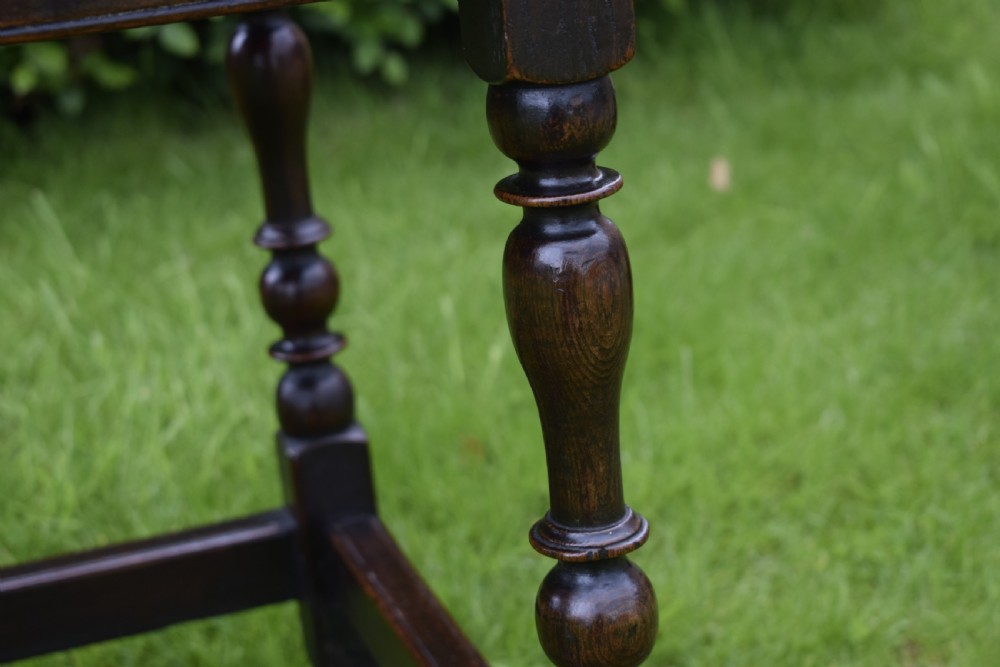 A dark oak 17th-century lowboy table featuring a carved rectangular top, a single carved drawer front with a central brass handle, turned legs, and low wooden stretchers. View XVII