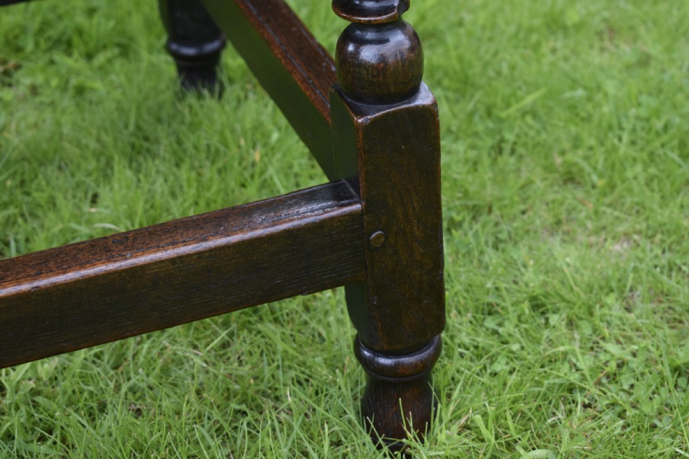 A dark oak 17th-century lowboy table featuring a carved rectangular top, a single carved drawer front with a central brass handle, turned legs, and low wooden stretchers. View XVIII