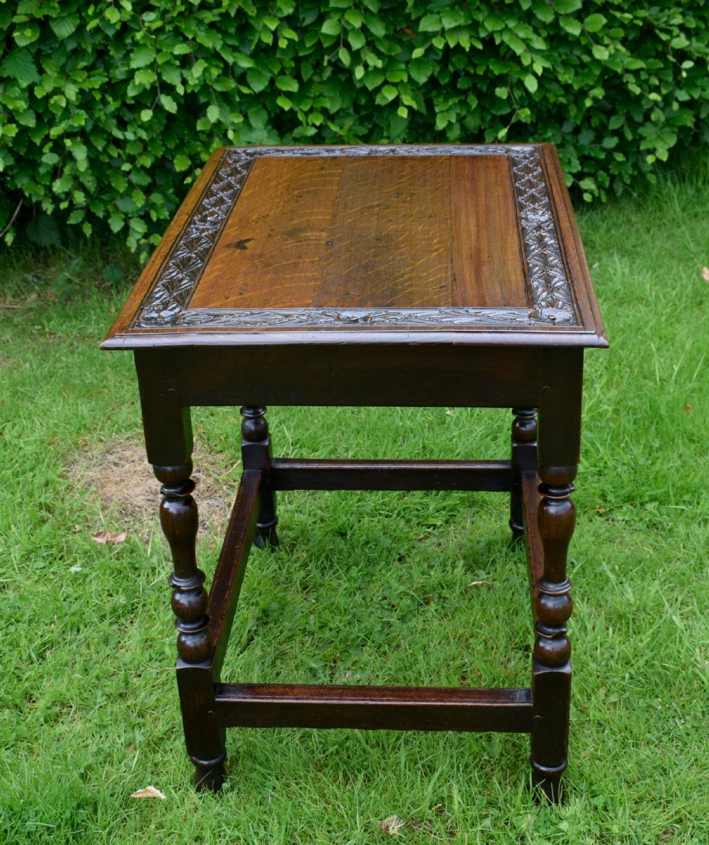 A dark oak 17th-century lowboy table featuring a carved rectangular top, a single carved drawer front with a central brass handle, turned legs, and low wooden stretchers. View XIX