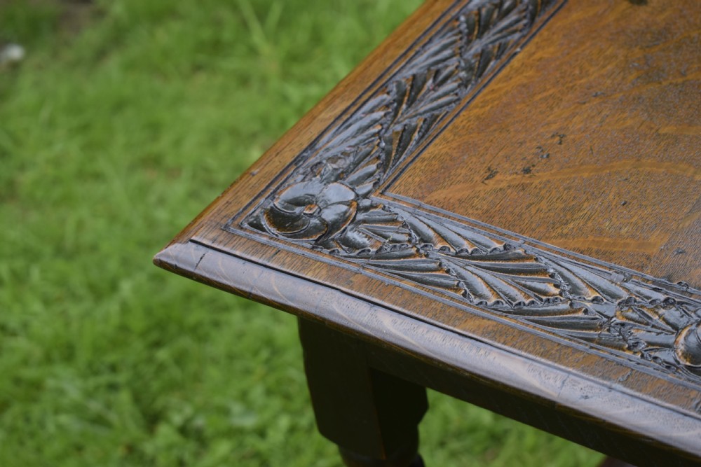 A dark oak 17th-century lowboy table featuring a carved rectangular top, a single carved drawer front with a central brass handle, turned legs, and low wooden stretchers. View XX