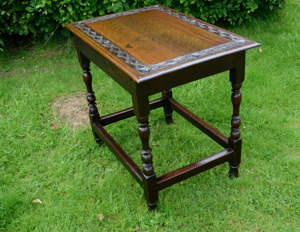 A dark oak 17th-century lowboy table featuring a carved rectangular top, a single carved drawer front with a central brass handle, turned legs, and low wooden stretchers. View XXII