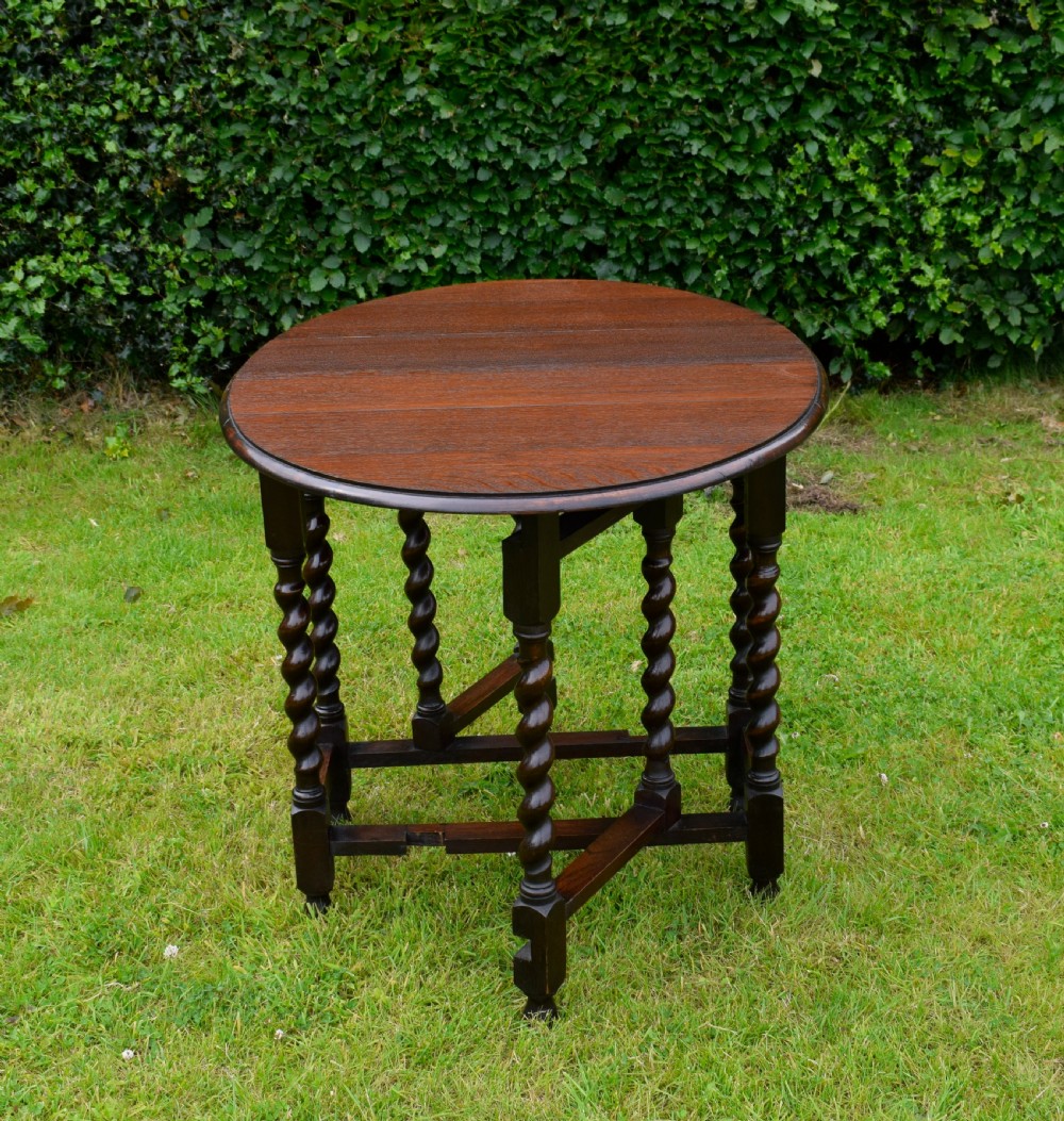 A dark oak round gateleg dining table featuring spirally turned barley twist legs and low stretchers.