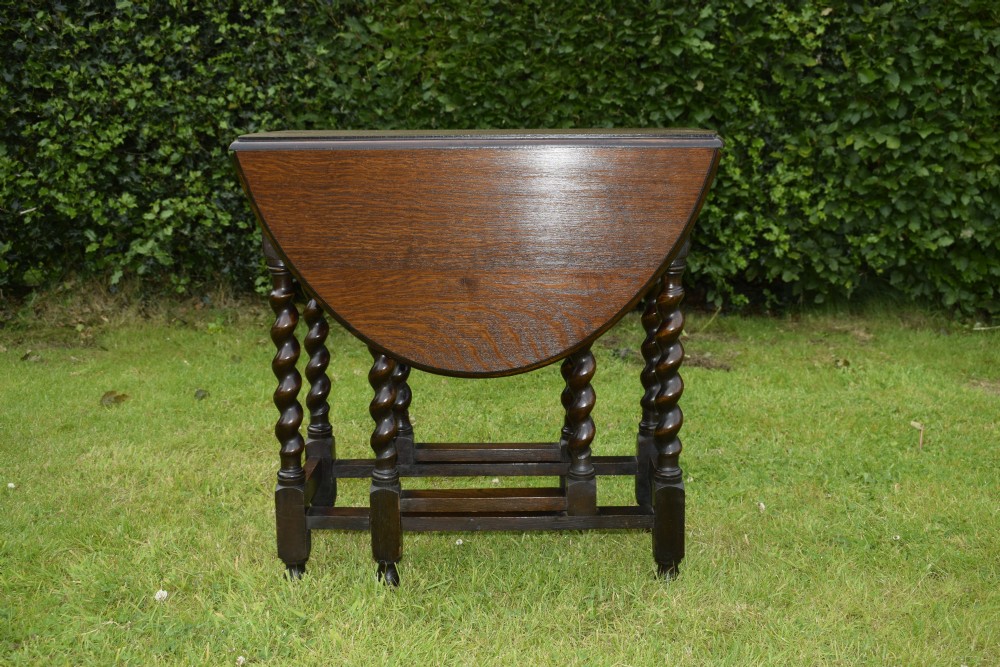 A dark oak round gateleg dining table featuring spirally turned barley twist legs and low stretchers. View IX