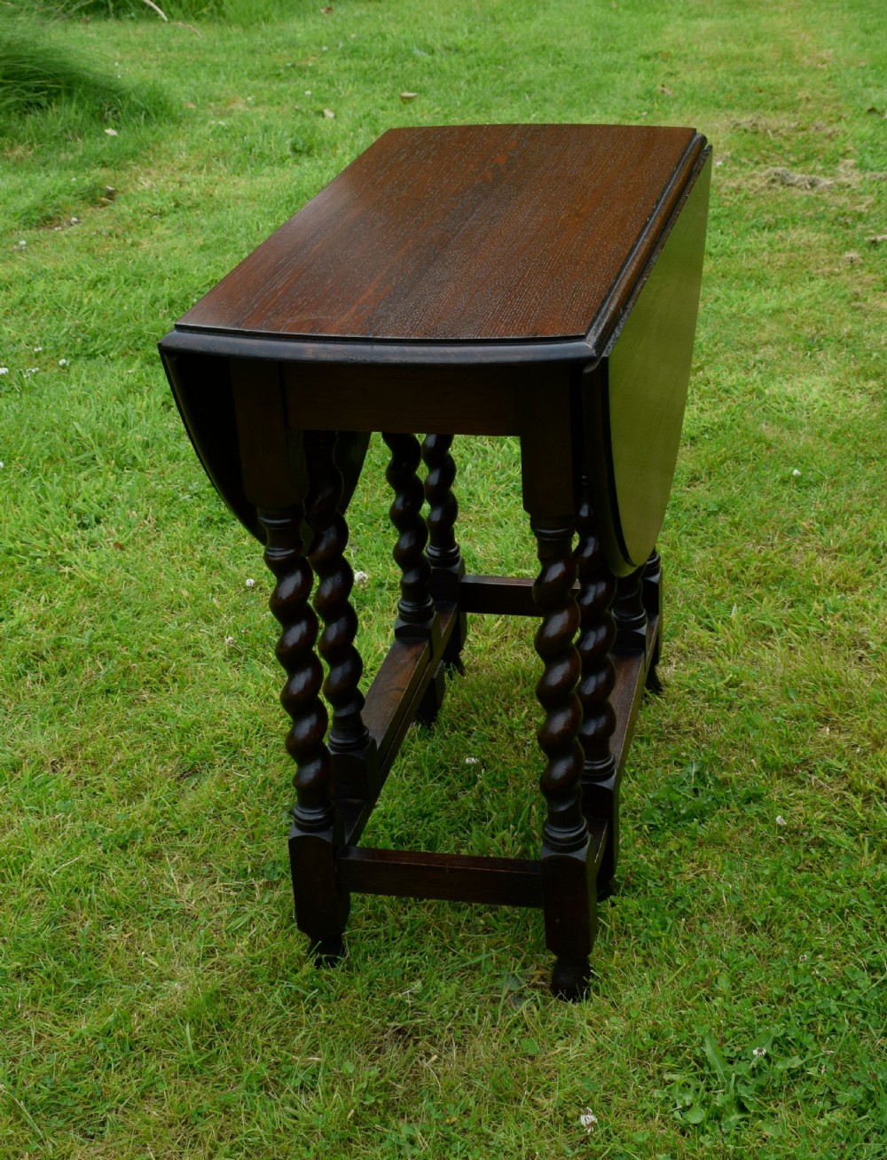 A dark oak round gateleg dining table featuring spirally turned barley twist legs and low stretchers. View XII