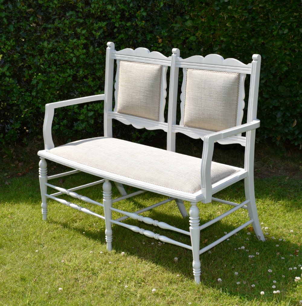 A white painted Edwardian two-seater bench featuring turned legs and neutral linen upholstered seat and back panels. View VI