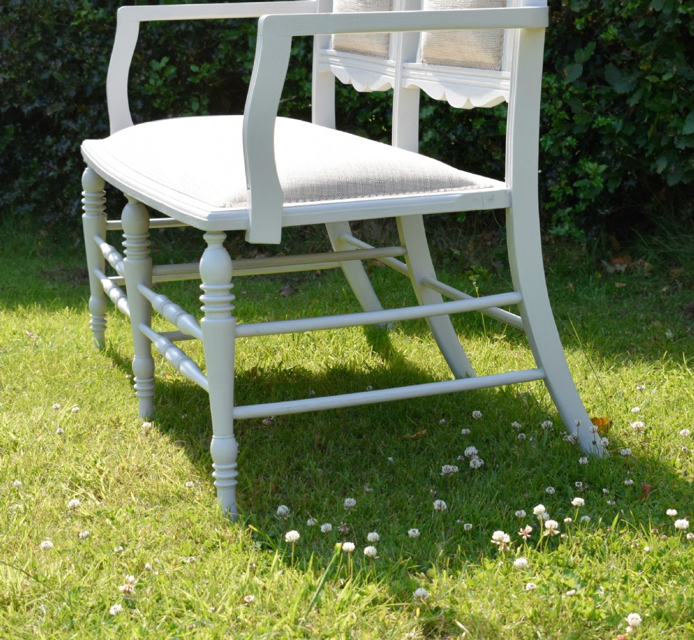 A white painted Edwardian two-seater bench featuring turned legs and neutral linen upholstered seat and back panels. View X
