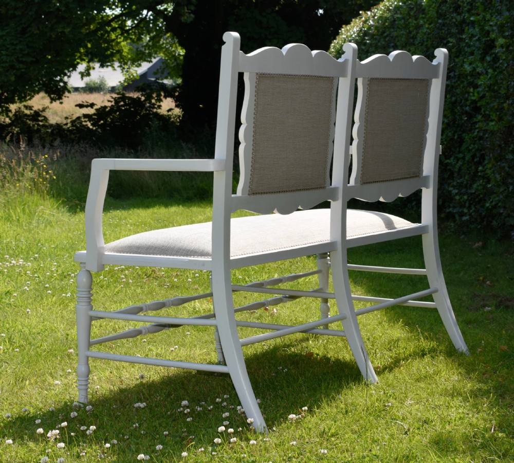 A white painted Edwardian two-seater bench featuring turned legs and neutral linen upholstered seat and back panels. View XIV