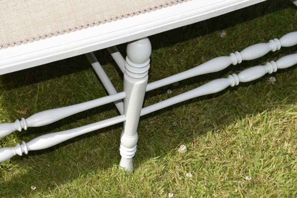 A white painted Edwardian two-seater bench featuring turned legs and neutral linen upholstered seat and back panels. View XIX