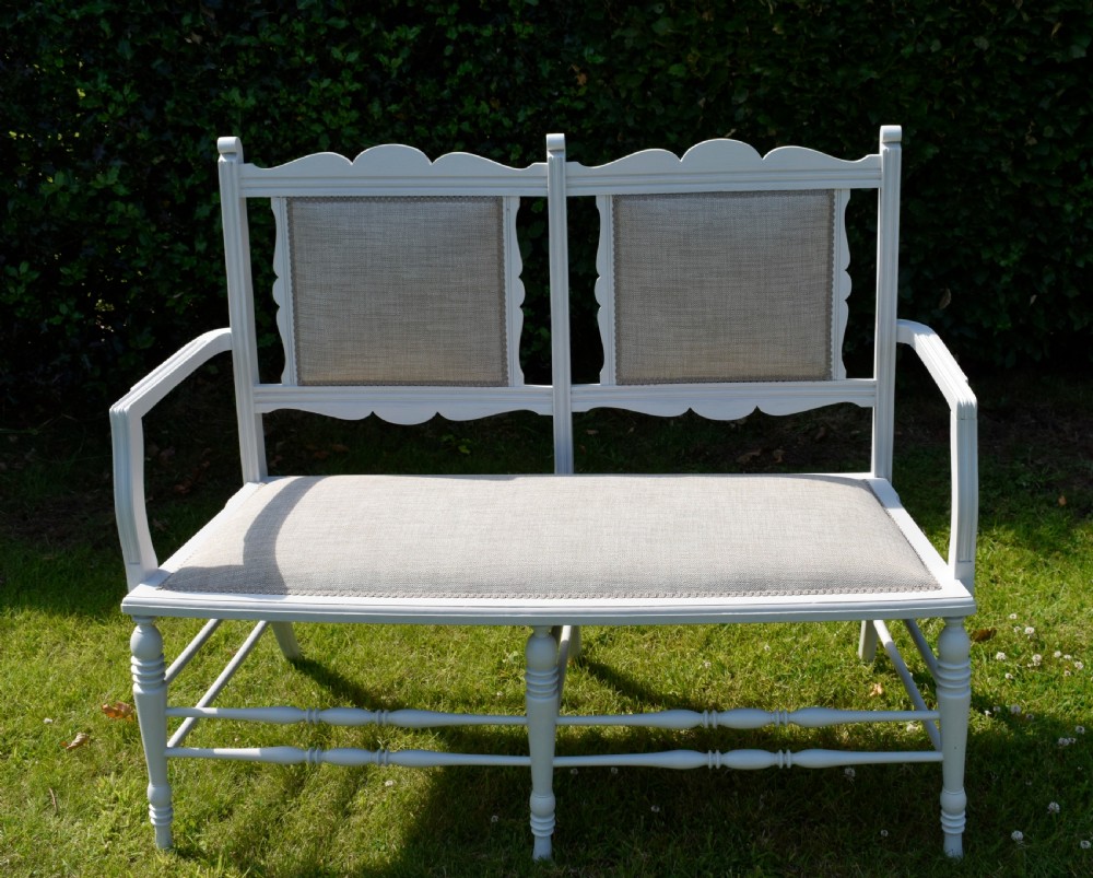 A white painted Edwardian two-seater bench featuring turned legs and neutral linen upholstered seat and back panels. View XX
