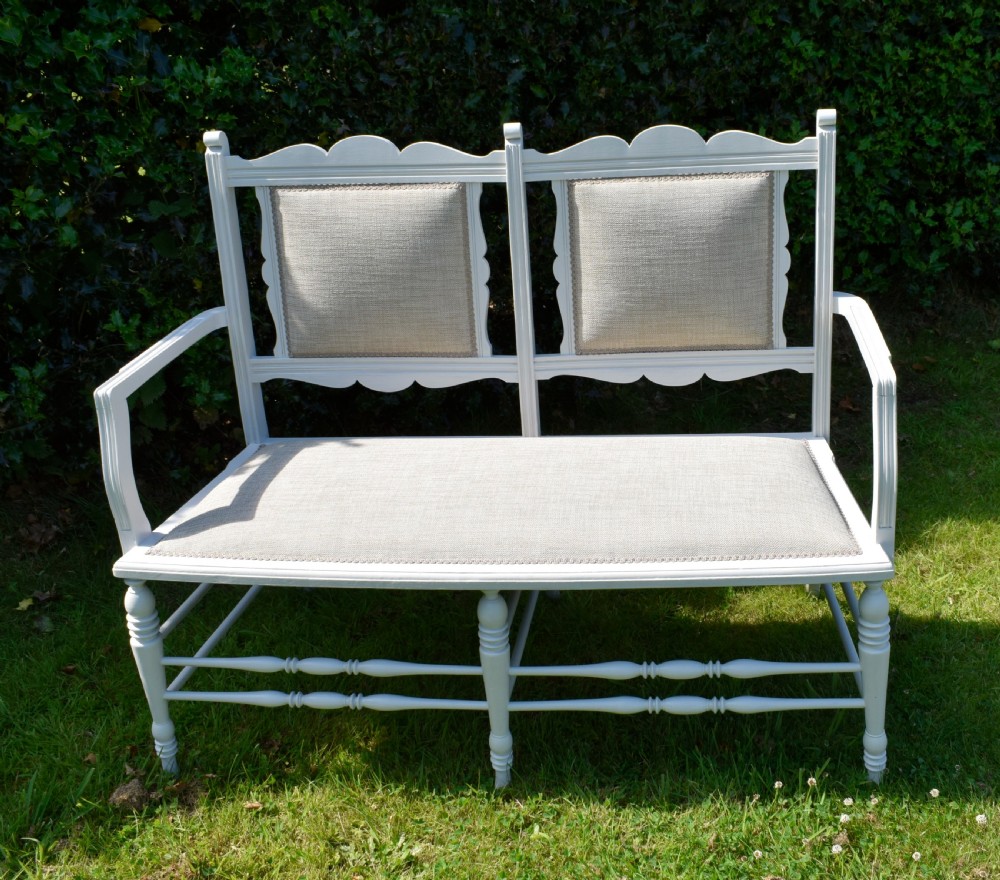 A white painted Edwardian two-seater bench featuring turned legs and neutral linen upholstered seat and back panels. View XXI