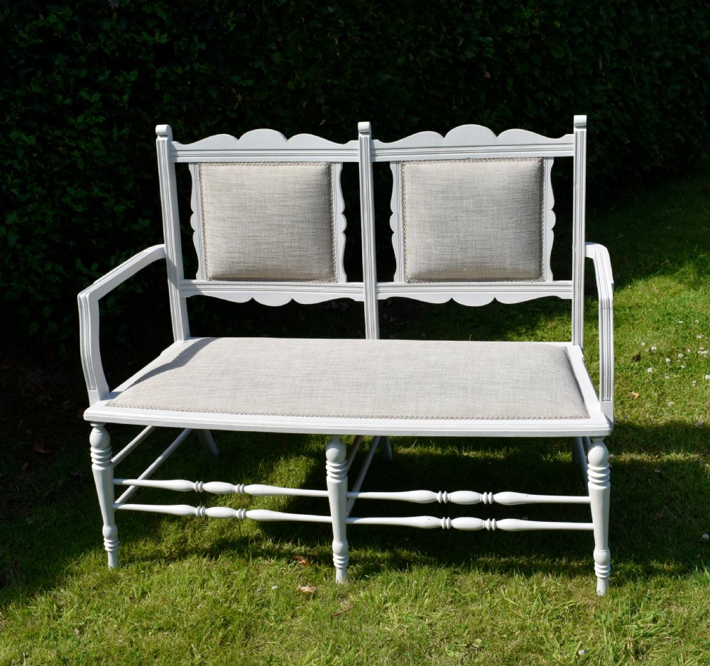 A white painted Edwardian two-seater bench featuring turned legs and neutral linen upholstered seat and back panels. View XXV