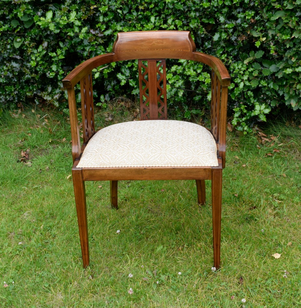 An Edwardian mahogany tub armchair featuring satinwood inlay, pierced lattice back splats, curved arms, and a light pattern-upholstered seat.