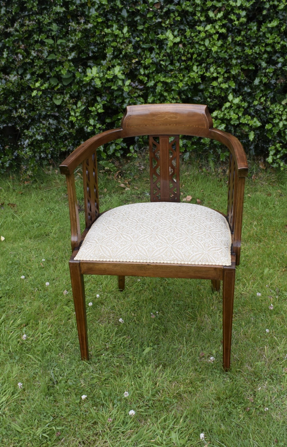 An Edwardian mahogany tub armchair featuring satinwood inlay, pierced lattice back splats, curved arms, and a light pattern-upholstered seat. View XII