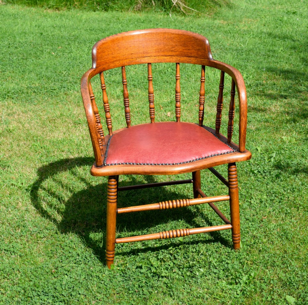 An antique oak captains chair featuring a curved horseshoe armrest, turned spindles, and a red leather upholstered seat finished with metal studding. View IV