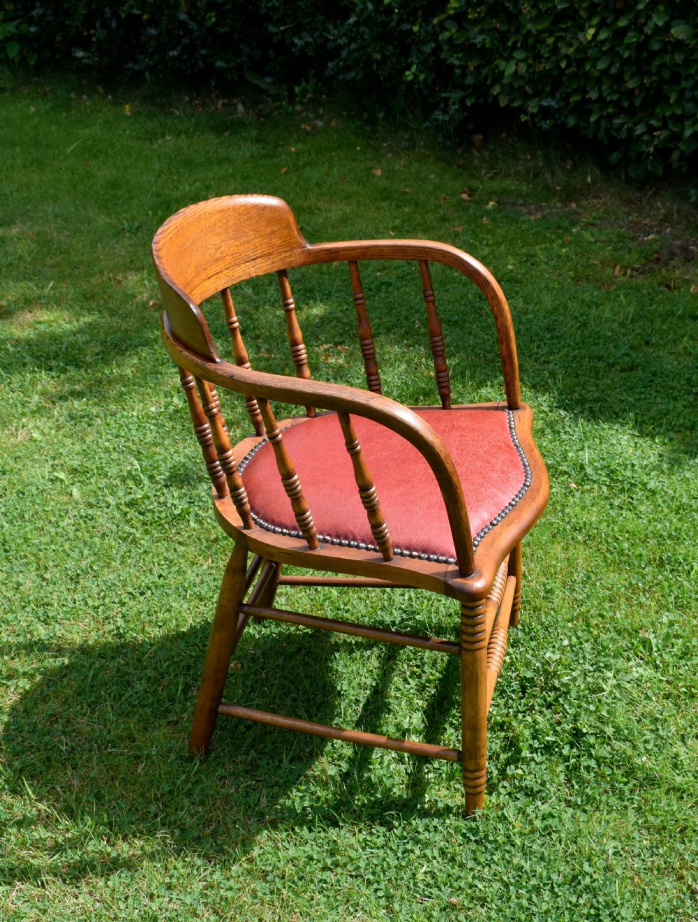 An antique oak captains chair featuring a curved horseshoe armrest, turned spindles, and a red leather upholstered seat finished with metal studding. View V