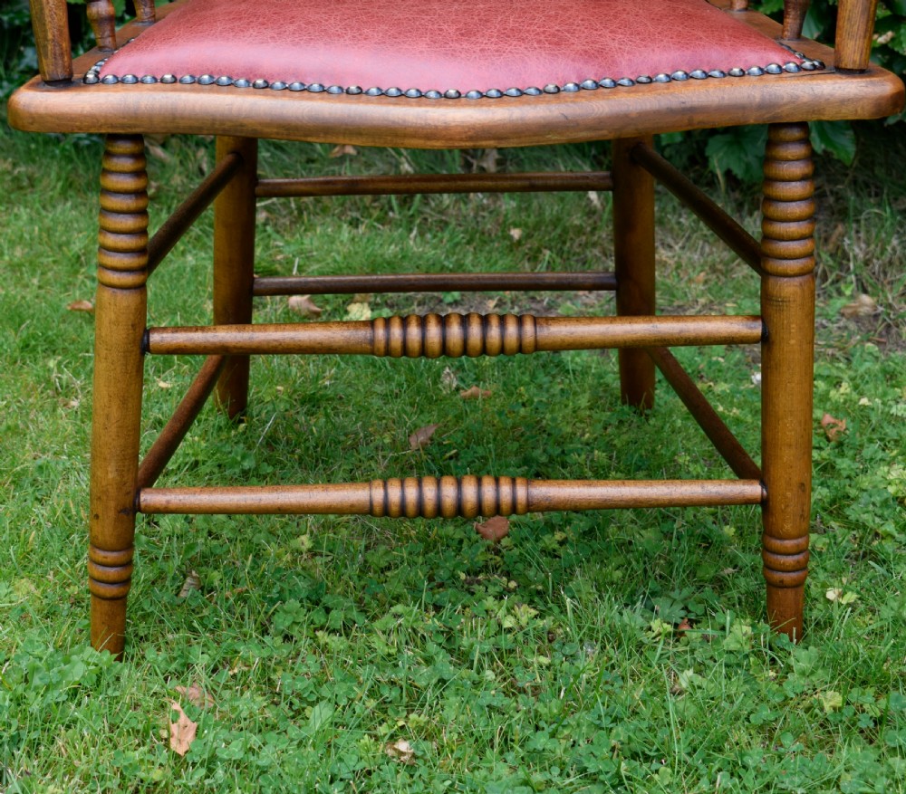 An antique oak captains chair featuring a curved horseshoe armrest, turned spindles, and a red leather upholstered seat finished with metal studding. View VII