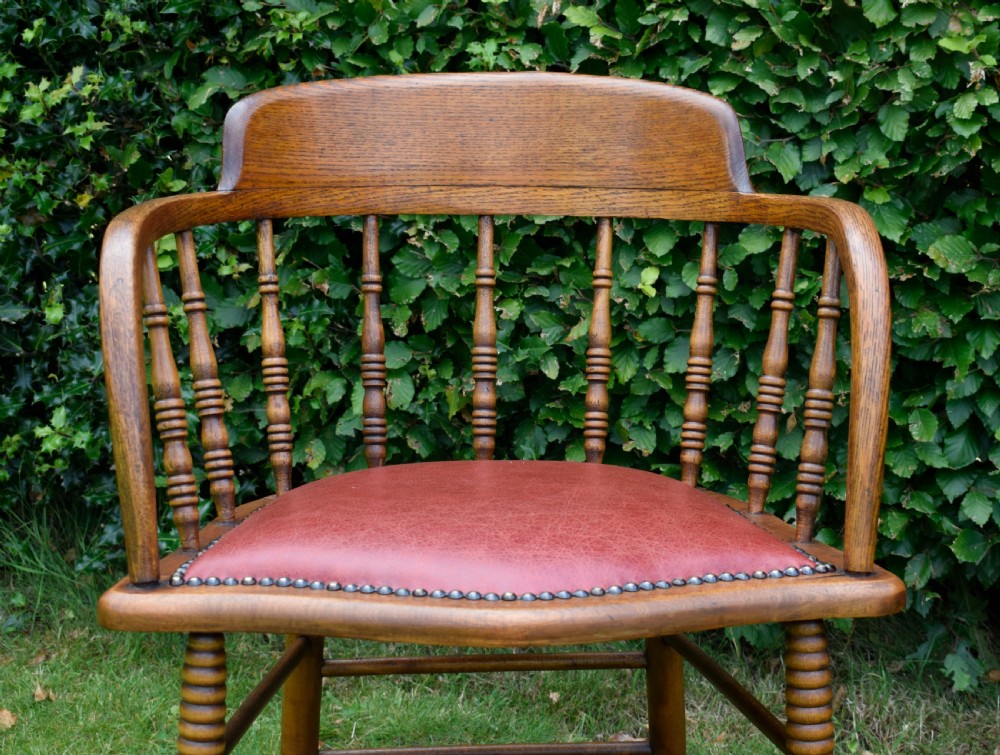 An antique oak captains chair featuring a curved horseshoe armrest, turned spindles, and a red leather upholstered seat finished with metal studding. View VIII