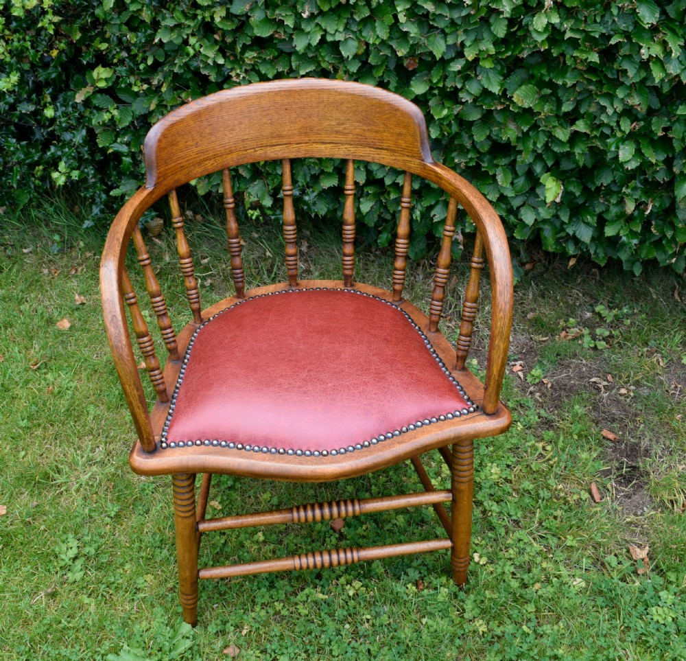 An antique oak captains chair featuring a curved horseshoe armrest, turned spindles, and a red leather upholstered seat finished with metal studding. View IX