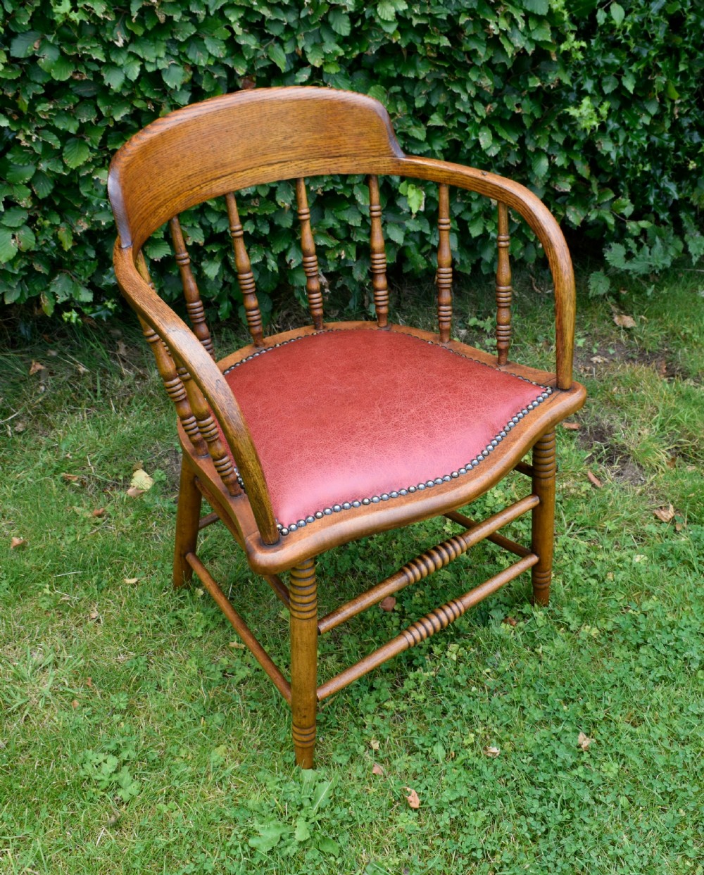 An antique oak captains chair featuring a curved horseshoe armrest, turned spindles, and a red leather upholstered seat finished with metal studding. View XI