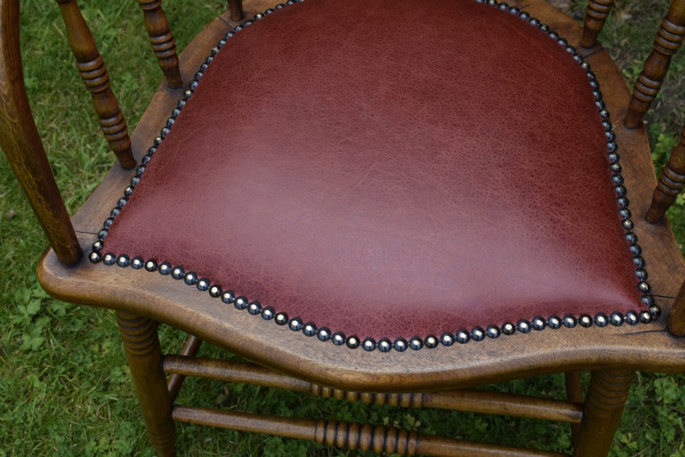 An antique oak captains chair featuring a curved horseshoe armrest, turned spindles, and a red leather upholstered seat finished with metal studding. View XIII