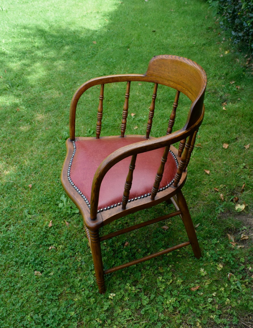 An antique oak captains chair featuring a curved horseshoe armrest, turned spindles, and a red leather upholstered seat finished with metal studding. View XIV