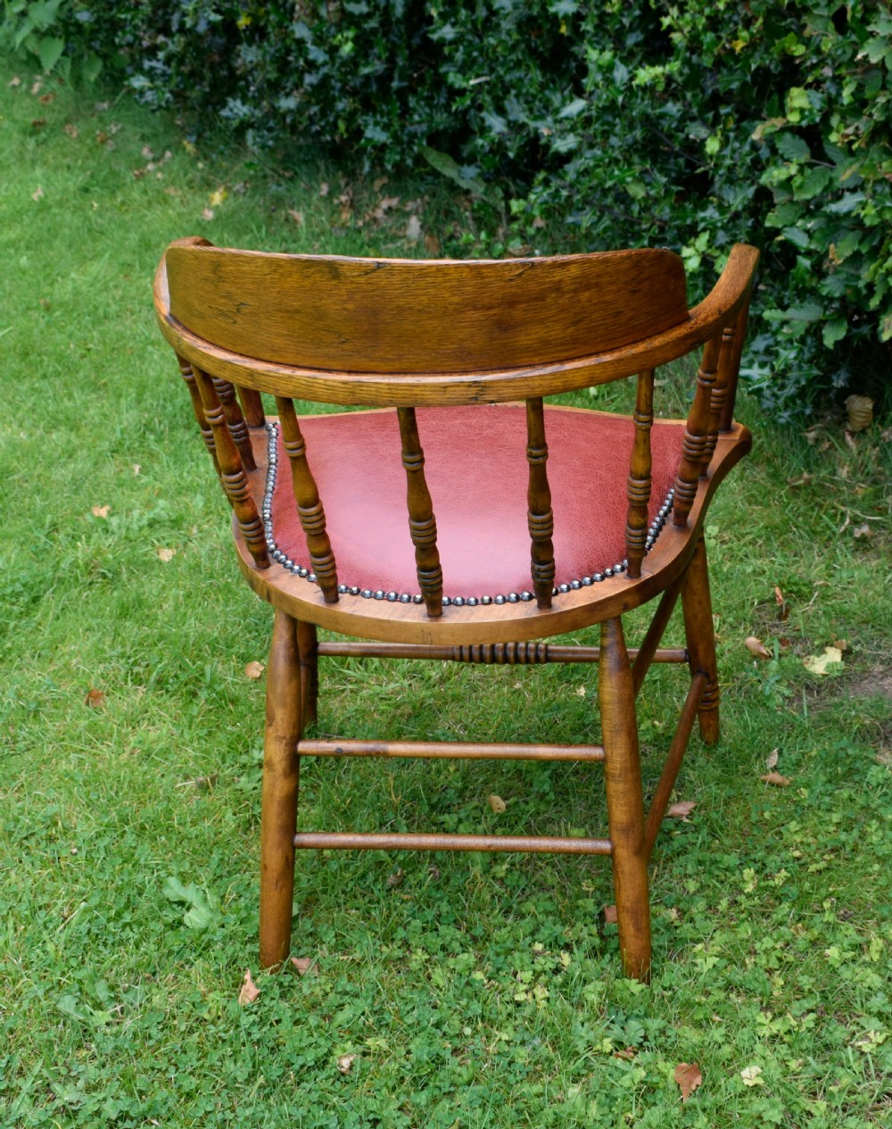 An antique oak captains chair featuring a curved horseshoe armrest, turned spindles, and a red leather upholstered seat finished with metal studding. View XV