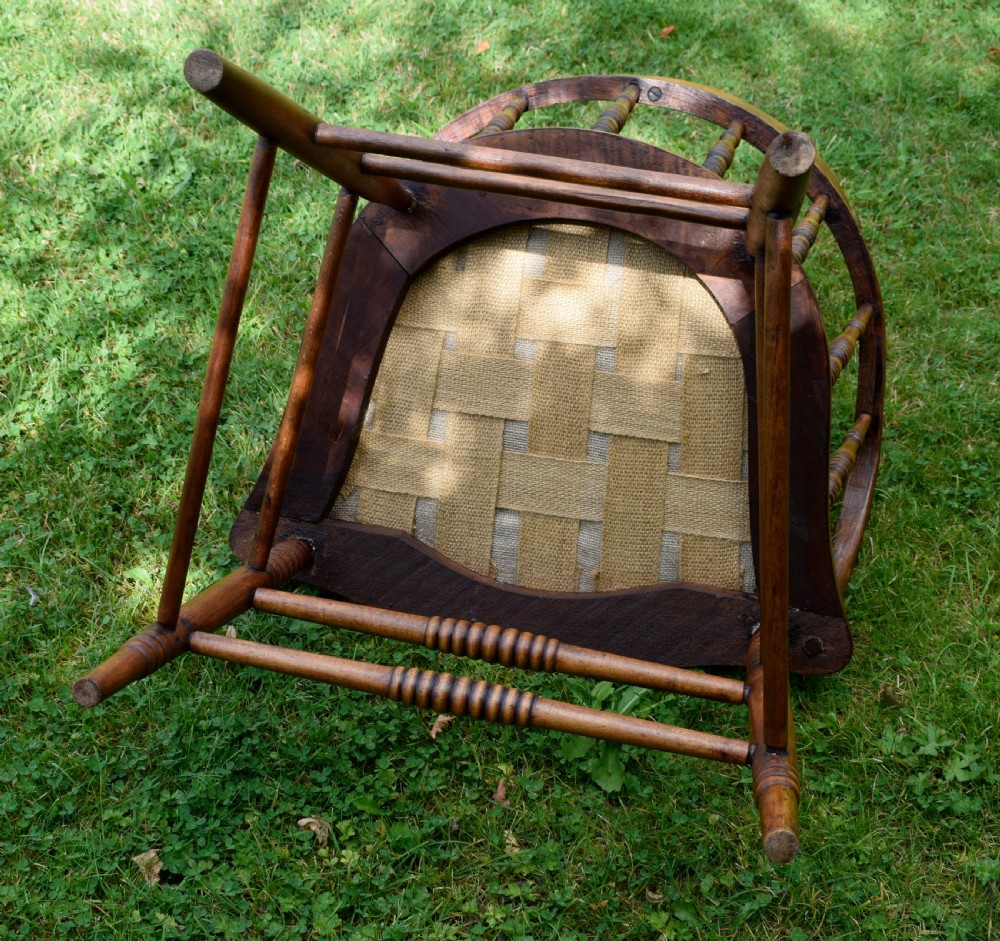An antique oak captains chair featuring a curved horseshoe armrest, turned spindles, and a red leather upholstered seat finished with metal studding. View XVI