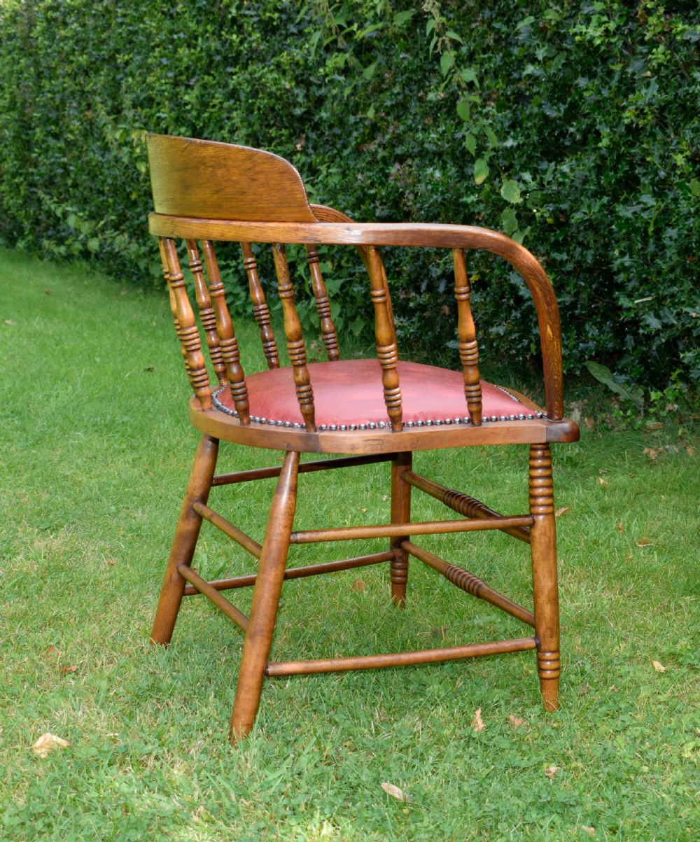 An antique oak captains chair featuring a curved horseshoe armrest, turned spindles, and a red leather upholstered seat finished with metal studding. View XVII
