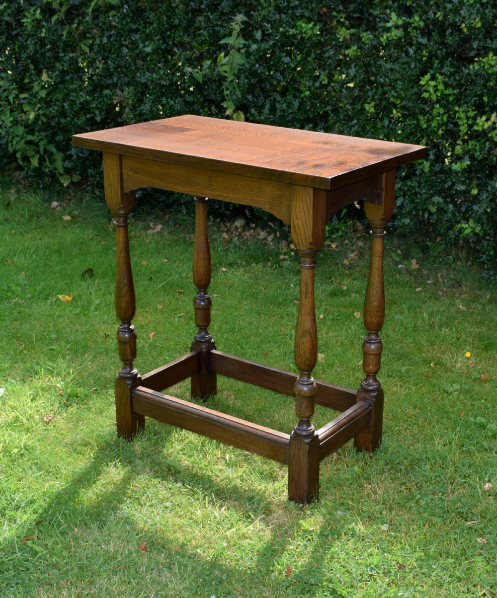 A tall rectangular dark oak side table featuring turned legs, a shaped apron, and lower perimeter box stretchers.