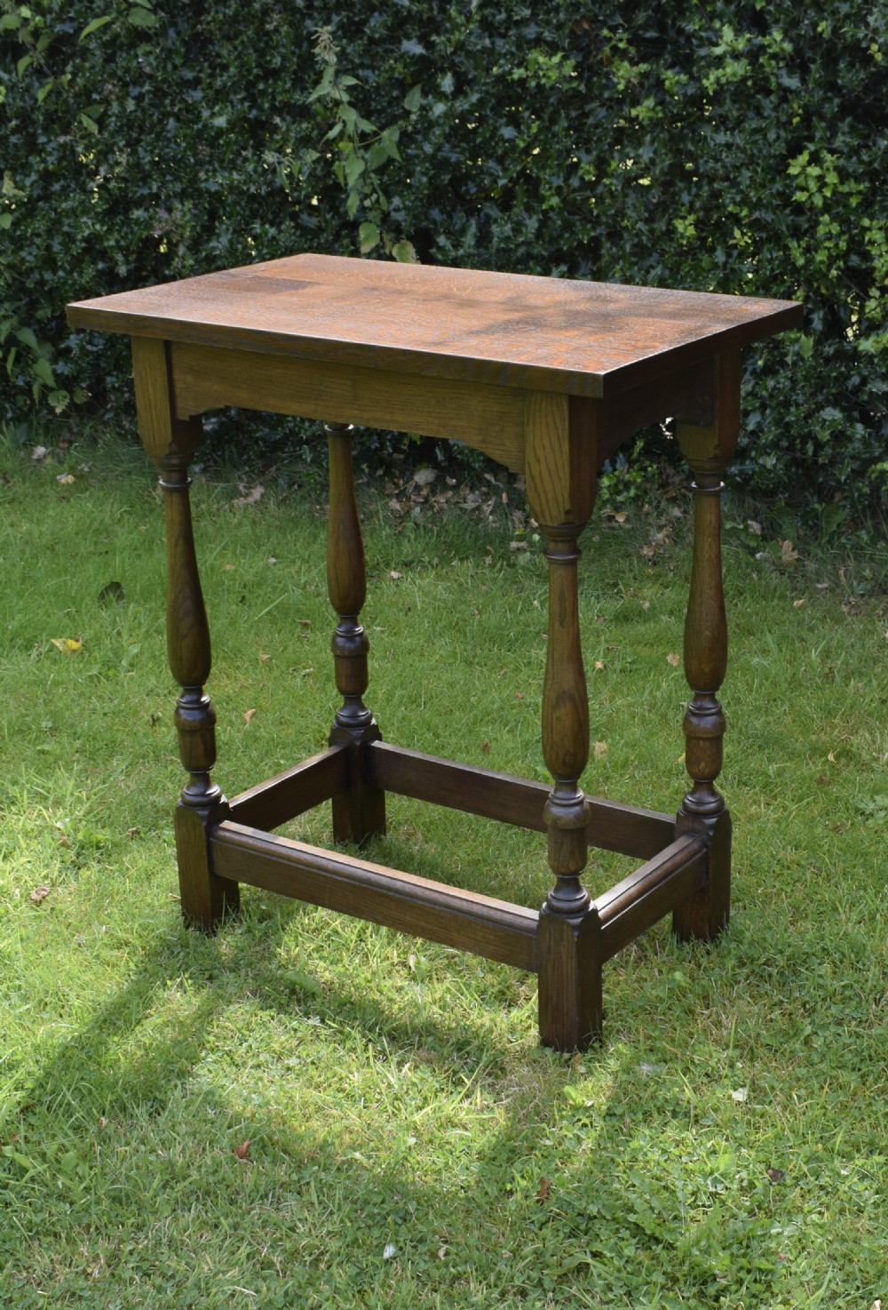 A tall rectangular dark oak side table featuring turned legs, a shaped apron, and lower perimeter box stretchers. View IX