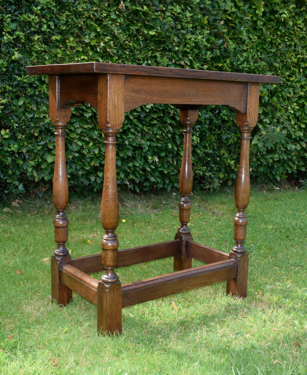 A tall rectangular dark oak side table featuring turned legs, a shaped apron, and lower perimeter box stretchers. View XV
