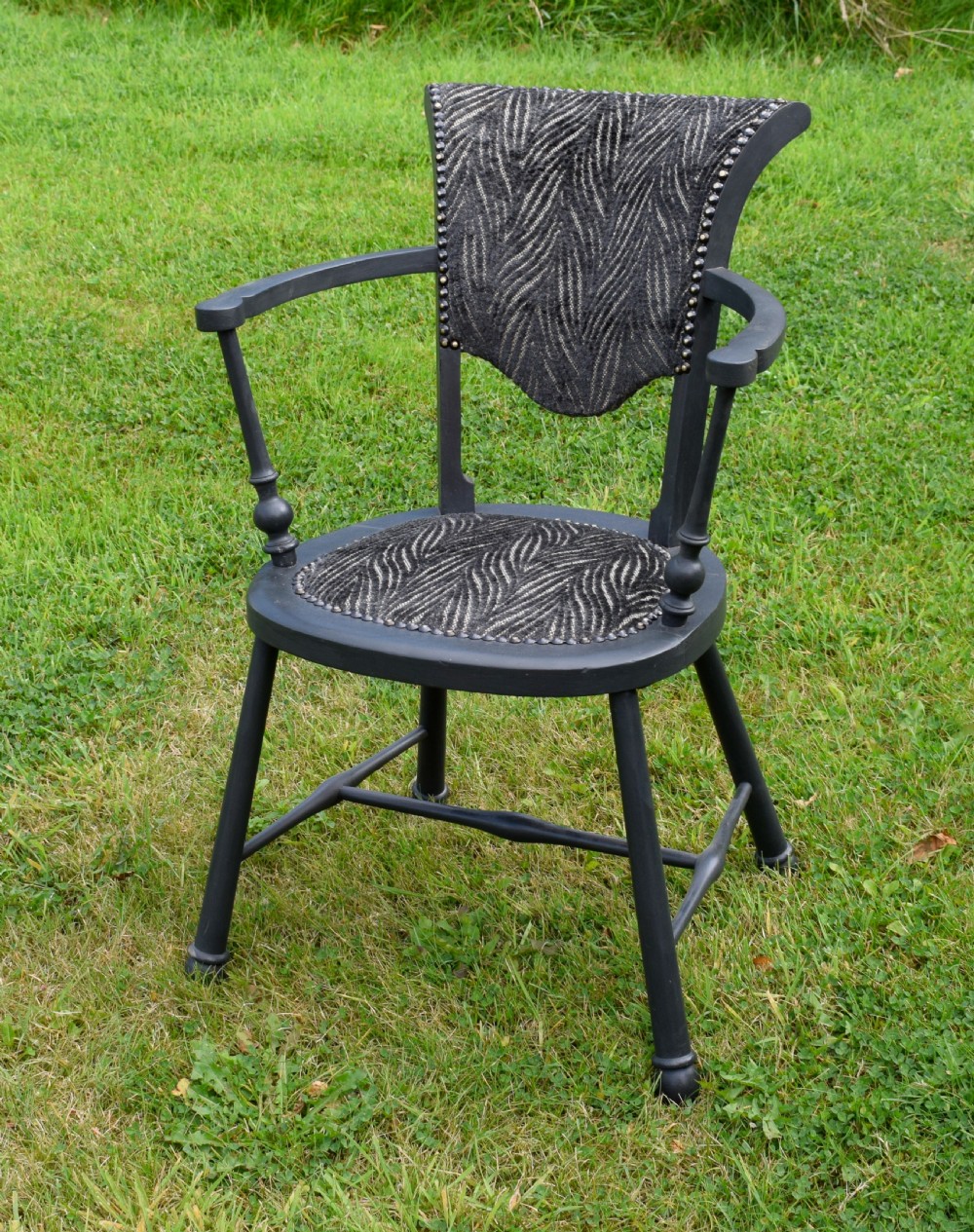 A dark grey painted Arts and Crafts style elbow chair featuring textured patterned fabric upholstery on the seat and curved backrest. View III