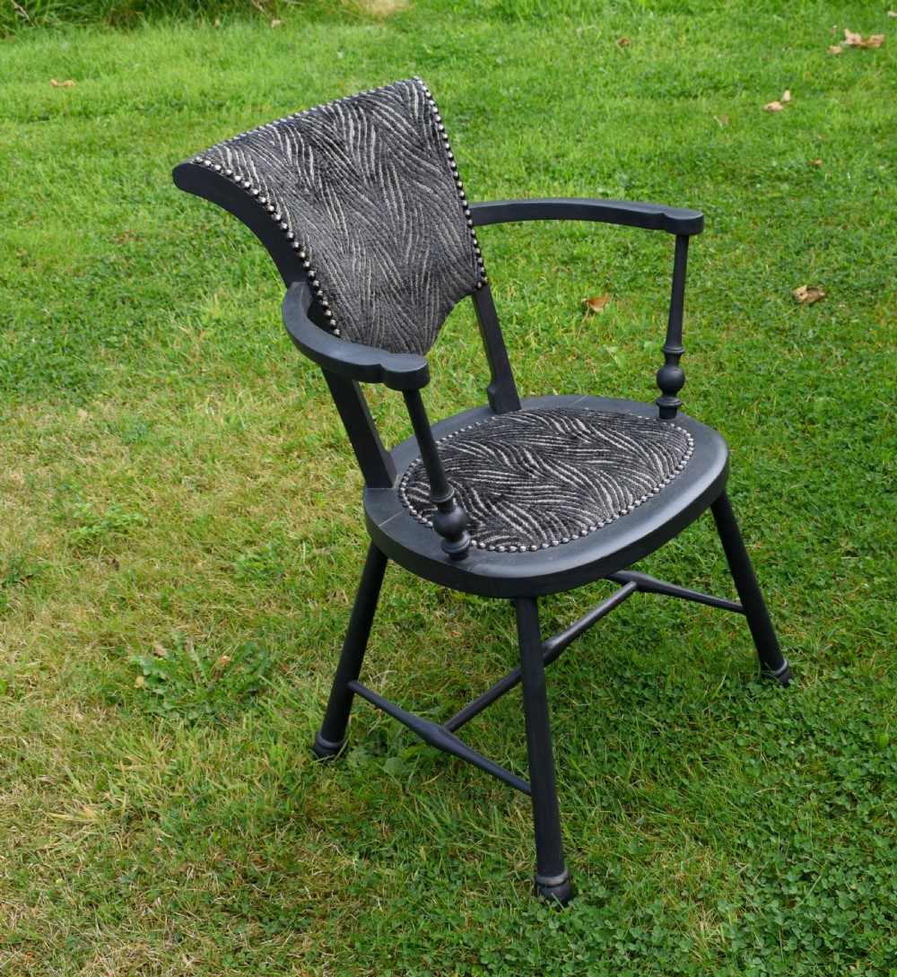 A dark grey painted Arts and Crafts style elbow chair featuring textured patterned fabric upholstery on the seat and curved backrest. View IV