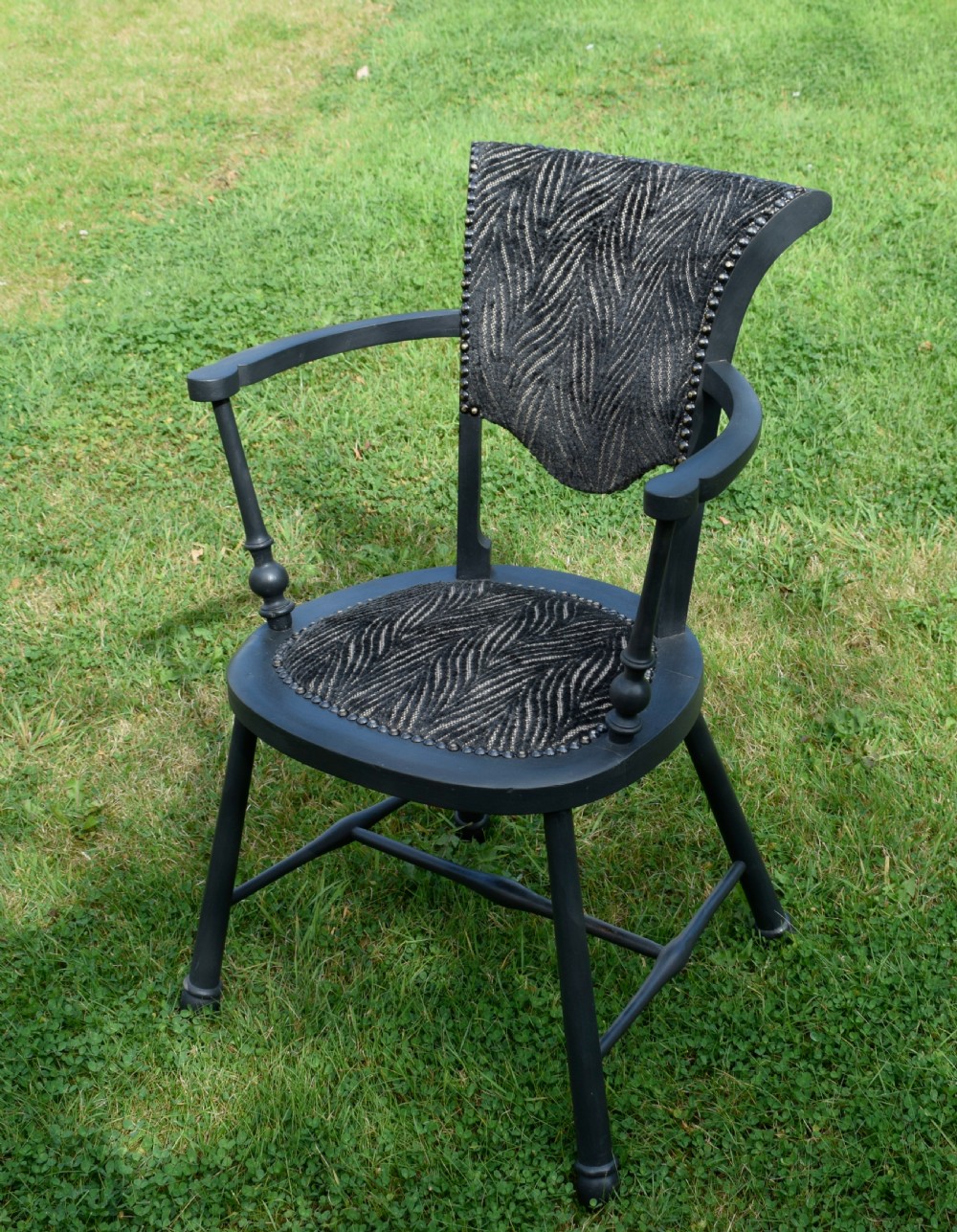 A dark grey painted Arts and Crafts style elbow chair featuring textured patterned fabric upholstery on the seat and curved backrest. View VI