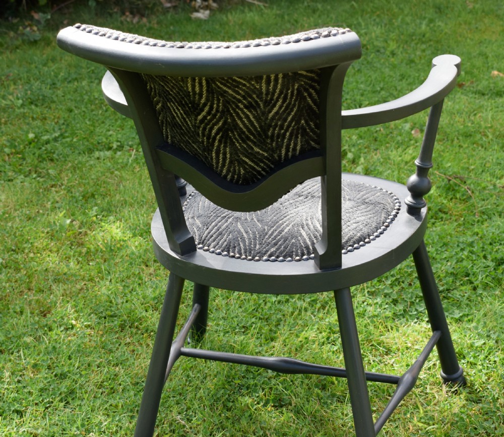 A dark grey painted Arts and Crafts style elbow chair featuring textured patterned fabric upholstery on the seat and curved backrest. View X