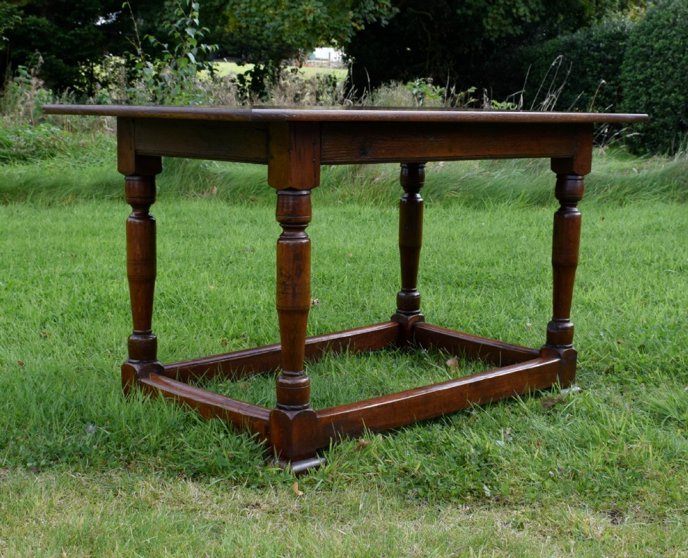 A rectangular dark oak refectory dining table featuring turned legs and a low perimeter stretcher base. View X