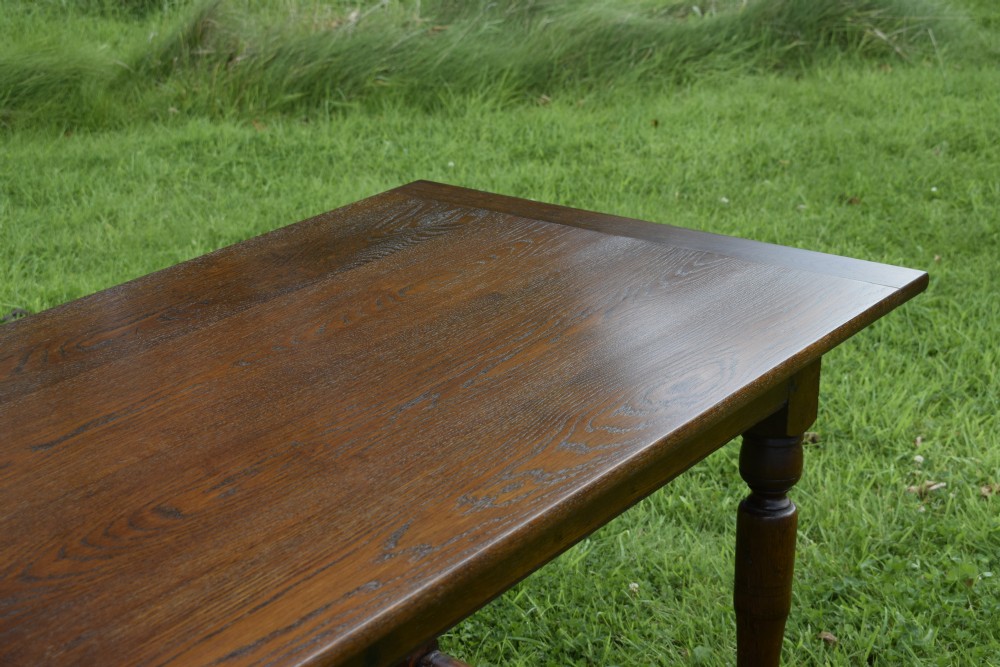 A rectangular dark oak refectory dining table featuring turned legs and a low perimeter stretcher base. View XV
