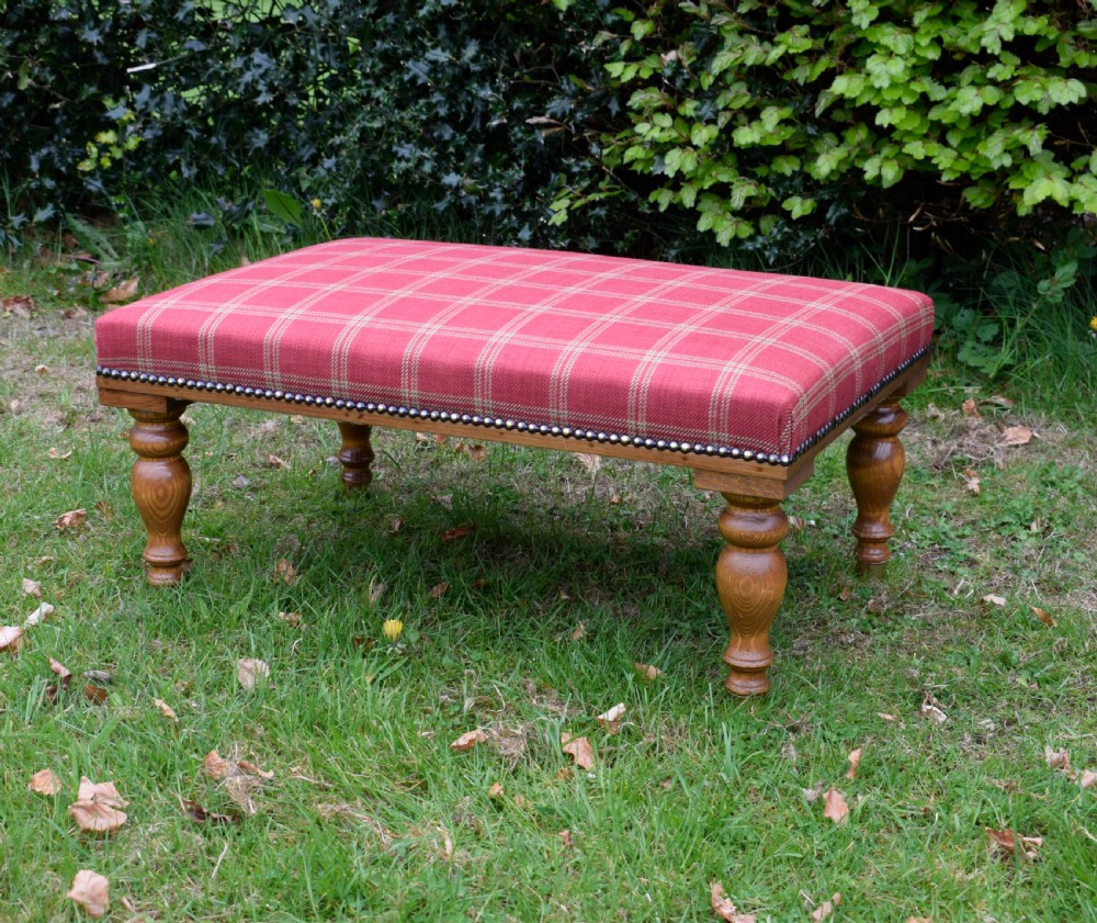 A large rectangular oak centre stool upholstered in red tartan fabric with turned legs and brass stud trimming.
