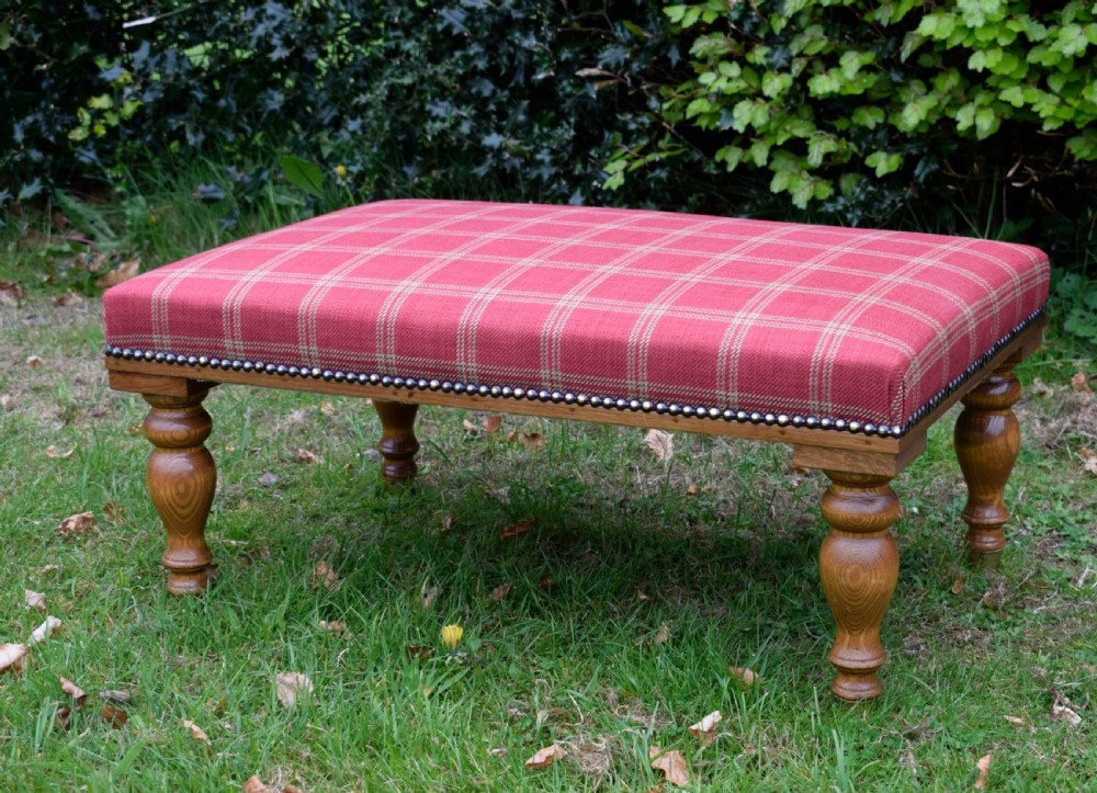 A large rectangular oak centre stool upholstered in red tartan fabric with turned legs and brass stud trimming. View VI