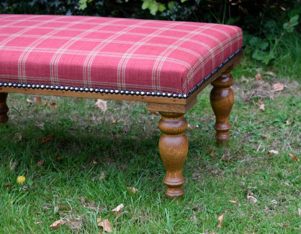 A large rectangular oak centre stool upholstered in red tartan fabric with turned legs and brass stud trimming. View VII