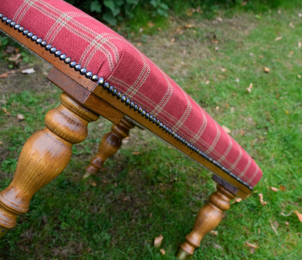 A large rectangular oak centre stool upholstered in red tartan fabric with turned legs and brass stud trimming. View VIII