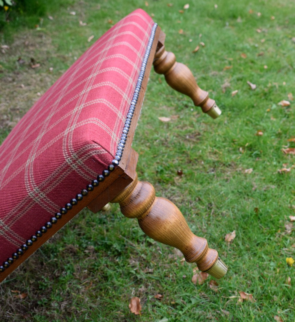 A large rectangular oak centre stool upholstered in red tartan fabric with turned legs and brass stud trimming. View IX