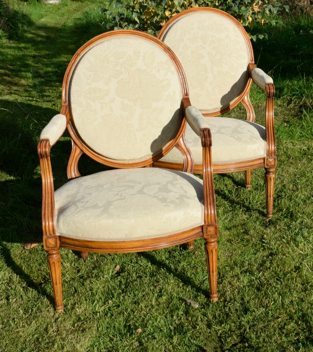 A pair of French Louis XVI style open armchairs featuring carved wooden frames, oval medallion backs, fluted legs, and cream damask upholstery. View VII