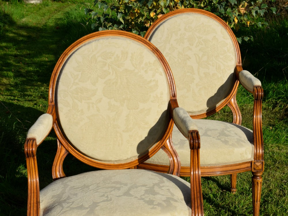 A pair of French Louis XVI style open armchairs featuring carved wooden frames, oval medallion backs, fluted legs, and cream damask upholstery. View VIII